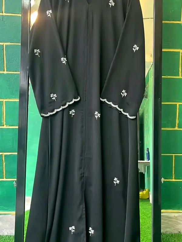 Black abaya with small white floral embroidery and scalloped cuffs, on a hanger