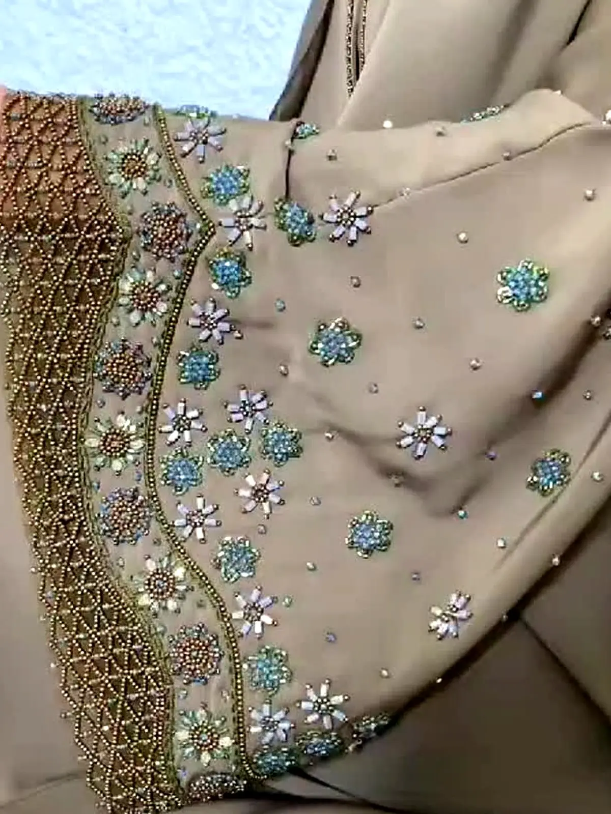 Close view of a taupe abaya sleeve with beaded floral work and a lattice border